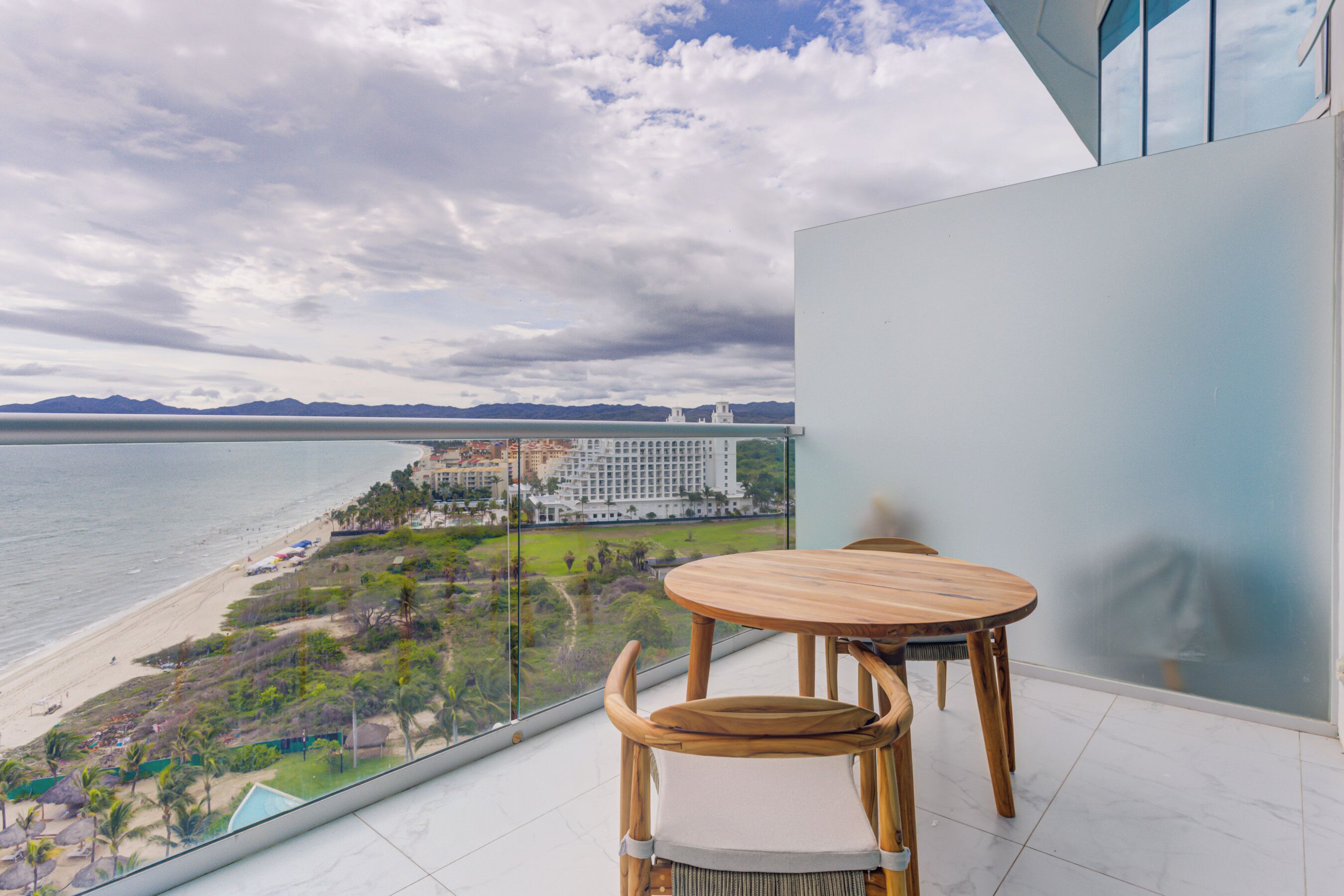 Un balcón con mesa y sillas de madera, con vistas a una playa y un hotel.