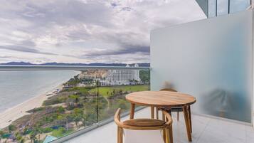 Un balcón con mesa y sillas de madera, con vistas a una playa y un hotel.