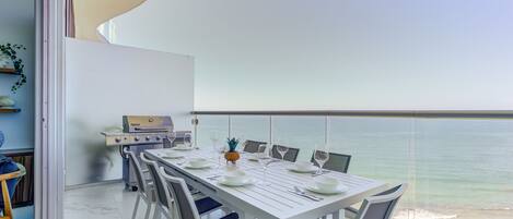 A dining area with a white table set for six, overlooking a beach.