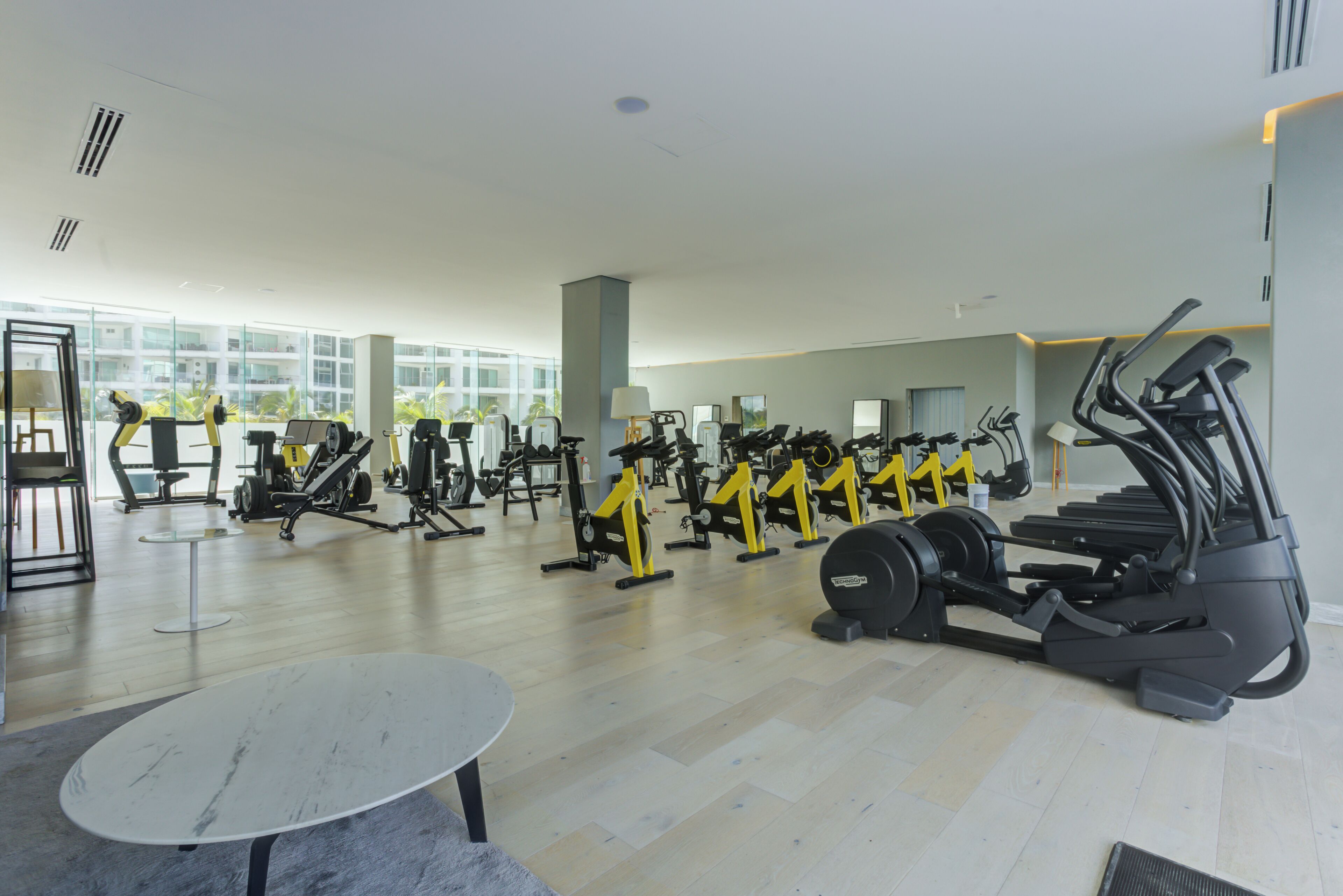 A spacious gym with various exercise equipment, large windows, and a marble table.