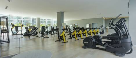 Une salle de sport spacieuse, dotée de divers appareils d’exercice, de grandes fenêtres et d’une table en marbre.