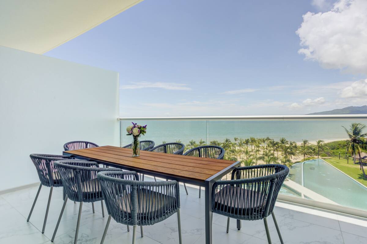 Un comedor con mesa de madera y sillas de mimbre, con vista a una piscina y una playa.
