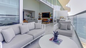 A modern living room with a grey sofa, a round coffee table, and a TV. There is a balcony with a view of the ocean. - Marítima Beachfront Playa Flamingos (Nuevo Nayarit)