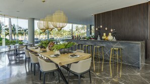 A modern dining area with a long wooden table, several chairs, and a bar counter with stools. - Marítima Beachfront Playa Flamingos (Nuevo Nayarit)