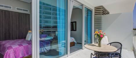 A modern room with a bed, a table with chairs, and a balcony with a view of buildings.