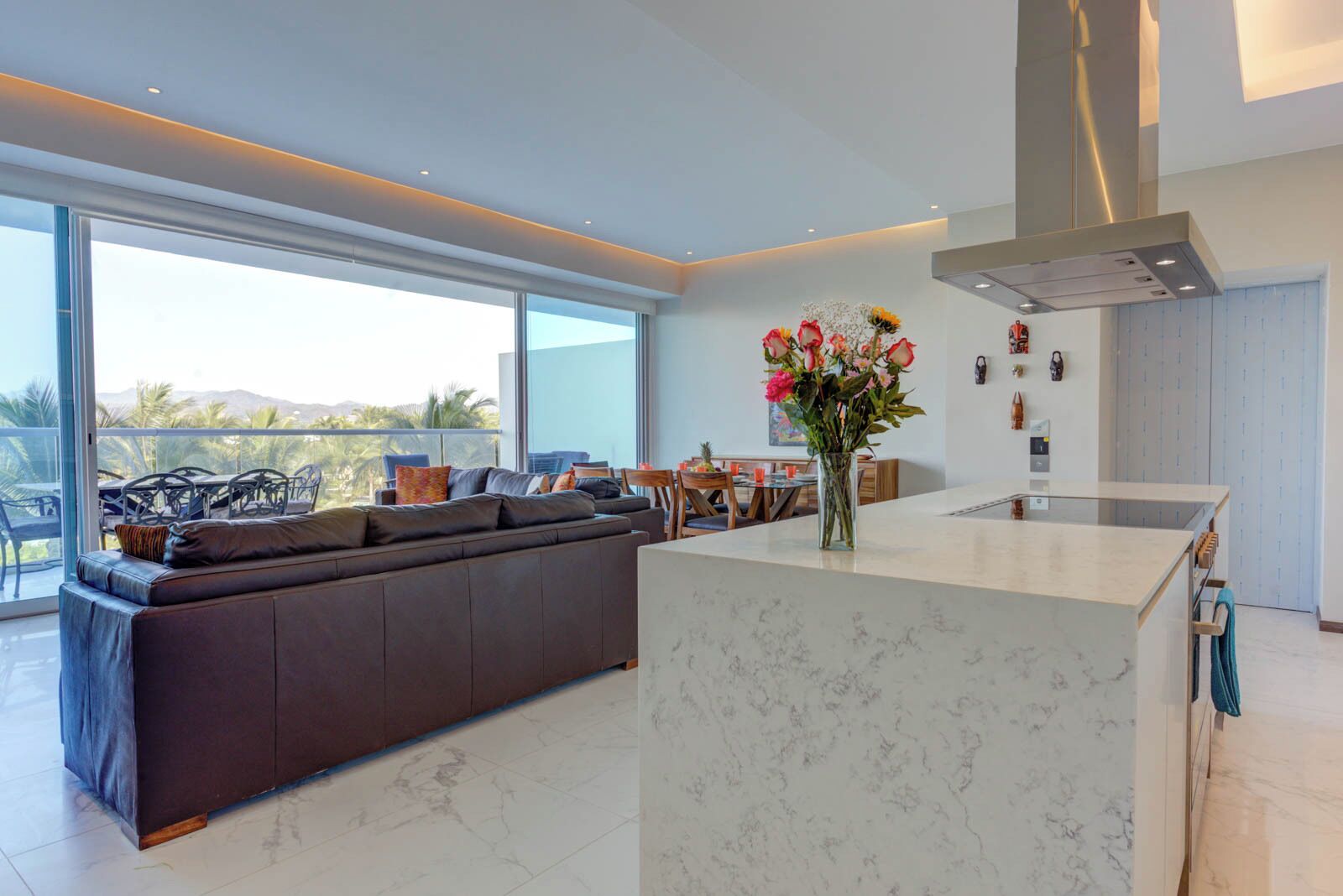 A modern kitchen with a marble countertop, a built-in oven, and a large window overlooking a balcony.