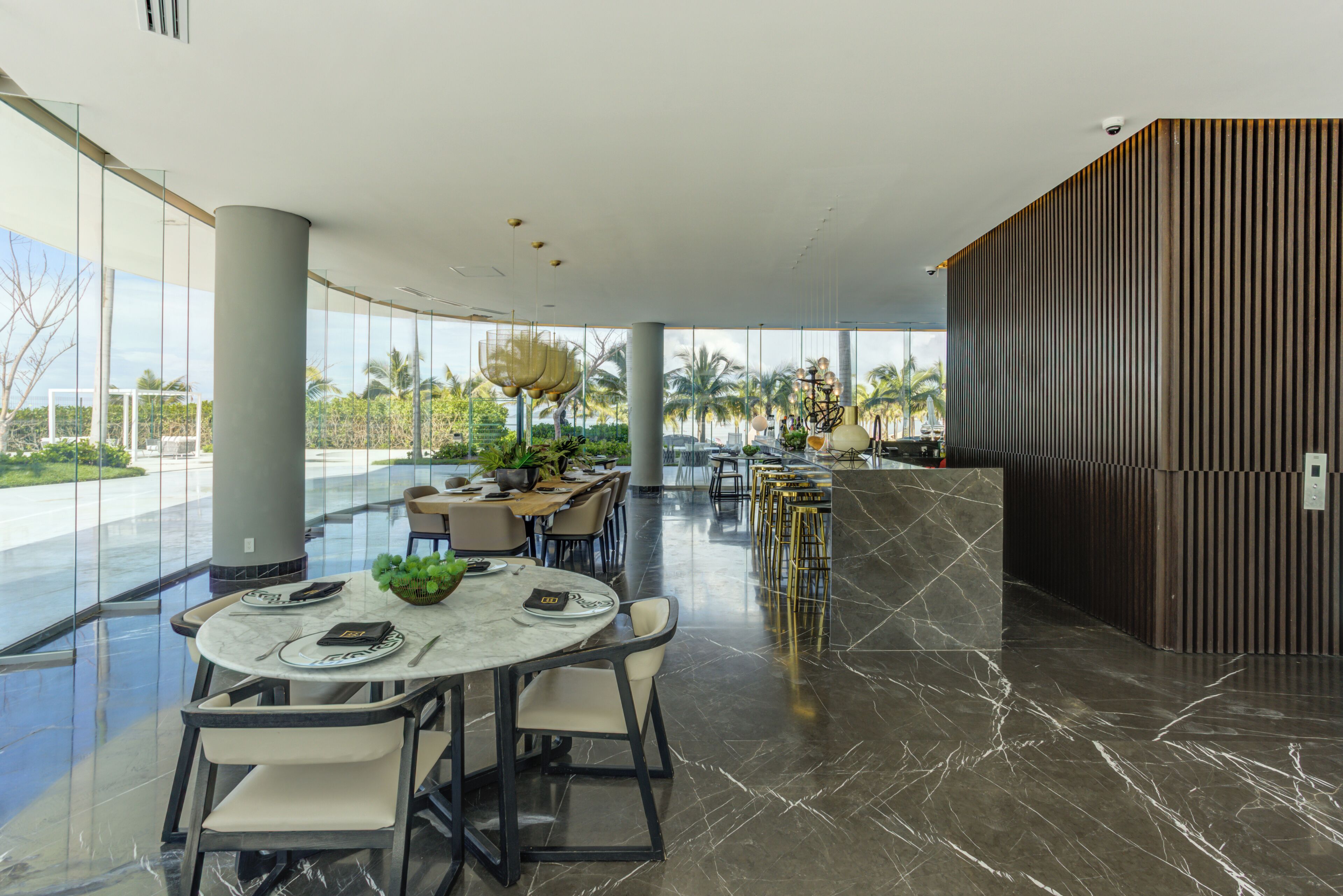 A modern dining area with round tables, chairs, and a view of palm trees.