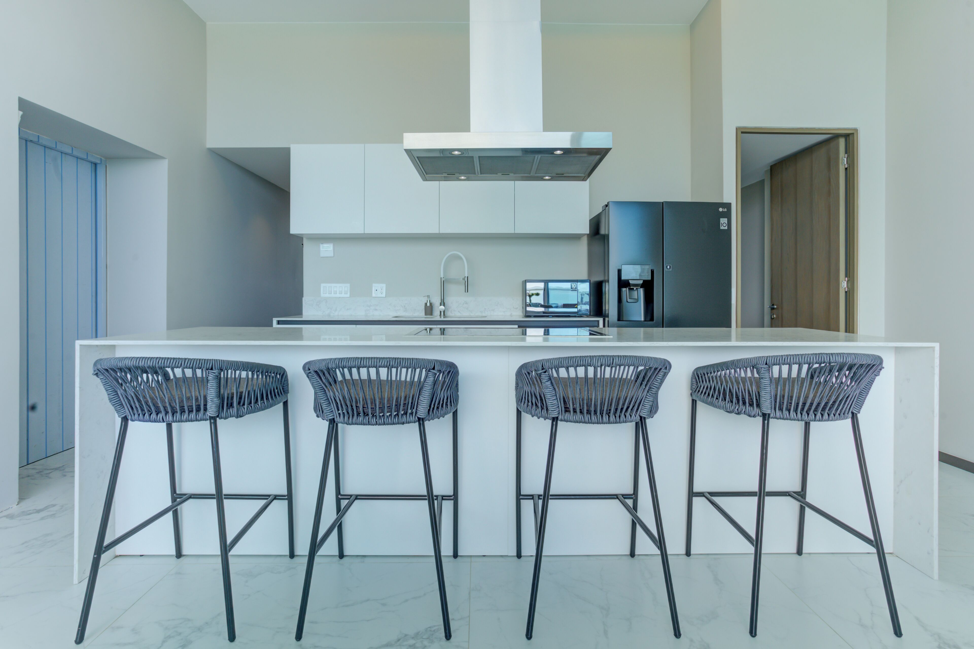 A modern kitchen with a central island, bar stools, a microwave, and a refrigerator.