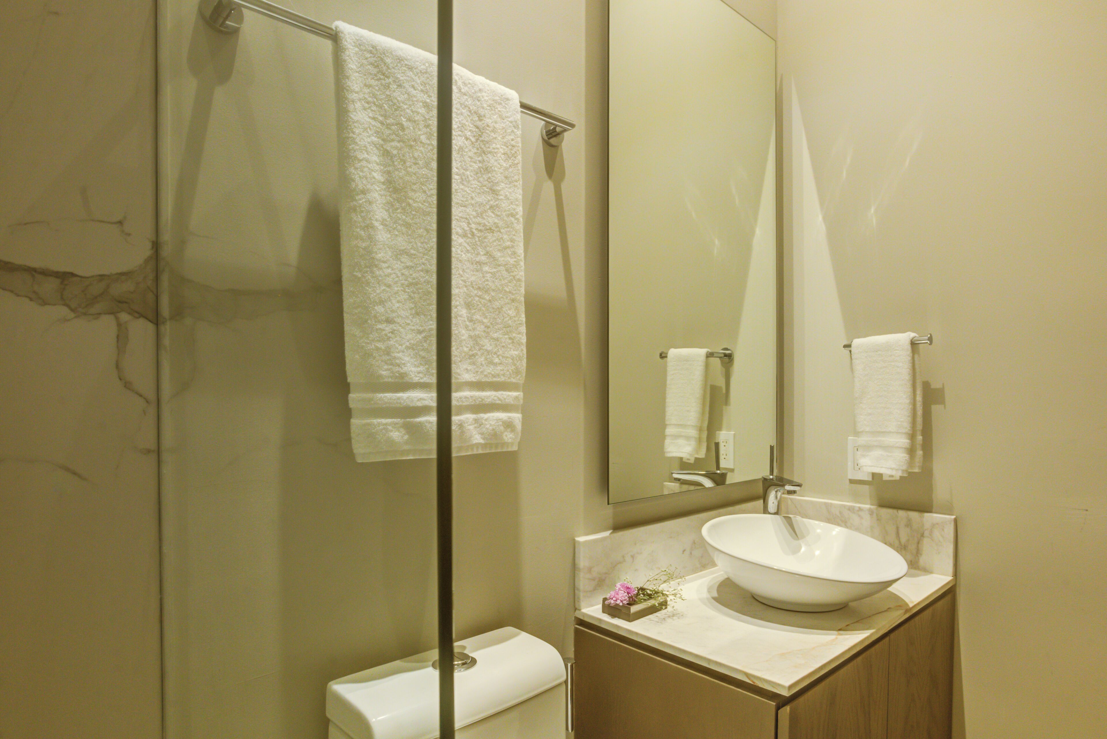 A bathroom with a marble sink, a glass shower enclosure, and a wooden vanity.