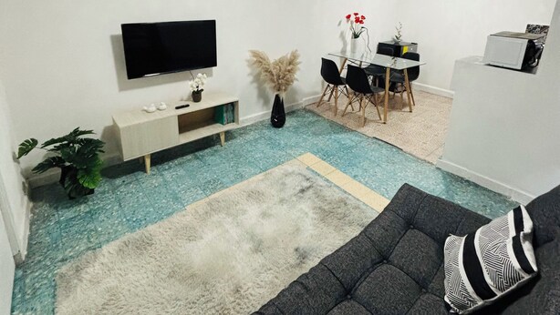 A modern living room with a black sofa, a flat-screen TV, a dining area with a table and chairs, and a small kitchen area with a microwave. - Safe and centrally located apartment (Ciudad de México)