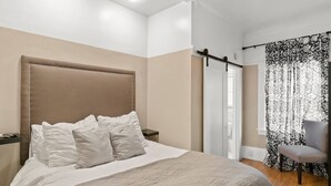 A bedroom with a large bed, a bedside table, a chair, a wardrobe, and a window with curtains.
