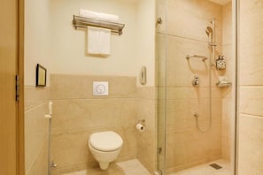 A small, modern bathroom with a toilet, a glass shower enclosure, and a towel rack. - Hotel Luxe Stay (New Delhi)