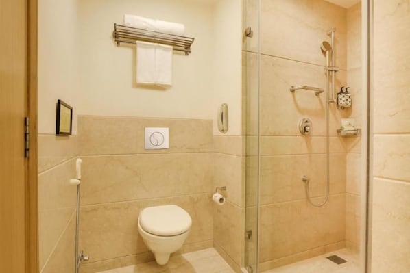 A small, modern bathroom with a toilet, a glass shower enclosure, and a towel rack. - Hotel Luxe Stay (New Delhi)