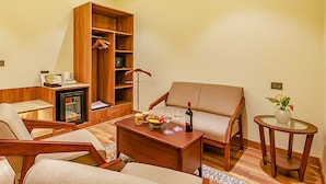 Un salon confortable avec un canapé, des fauteuils, une table basse, une bibliothèque, un petit réfrigérateur et une table d’appoint agrémentée d’une plante.
