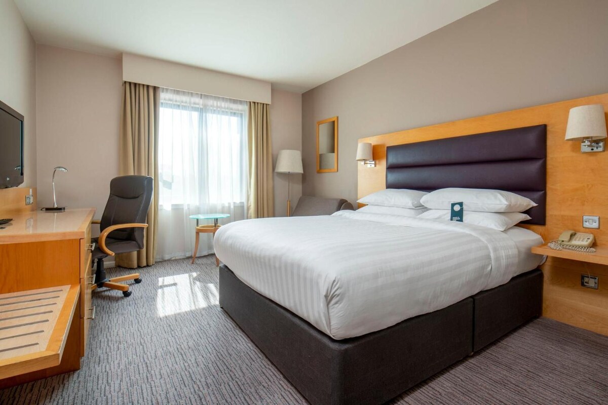 Une chambre d’hôtel avec un grand lit, un bureau avec une chaise, une petite table, une lampe et un téléviseur.