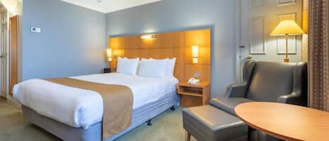 Camera d'albergo con un letto grande, comodini, una scrivania, una sedia e una lampada.