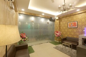 A modern lobby with a glass partition, a chandelier, a sofa, and a fireplace. - Hotel Luxe Stay (New Delhi)