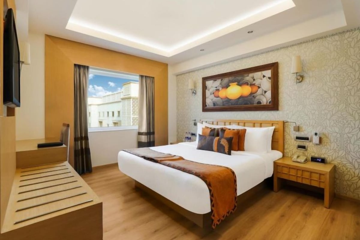 A hotel room with a bed, bedside table, lamp, and a painting on the wall.