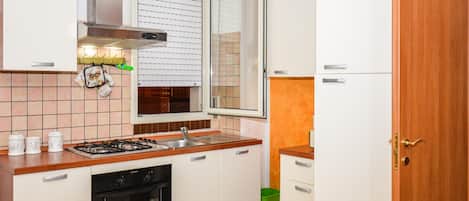 Cocina compacta con estufa a gas, horno y ventana con persianas.