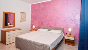 A bedroom with a large bed, a dresser, two bedside tables with lamps, and a pink textured wall. - 2 bedroom beautiful apartment in Pozzallo (Pozzallo)