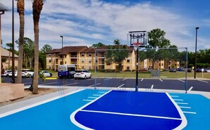 A basketball court with a blue surface, surrounded by a chain-link fence, and a basketball hoop.