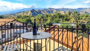 A balcony with a table, a bottle of wine, and a glass. The balcony overlooks a mountainous landscape with greenery and a clear sky. - 2 bedroom gorgeous apartment in Trappitello (Trappitello)
