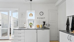 A kitchen with white cabinets, a sink, a clock, and a window with a wicker basket.