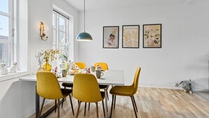 A modern dining area with a white table, yellow chairs, and a pendant light.