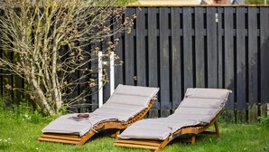 Two wooden lounge chairs with grey cushions and a pair of sunglasses on one.