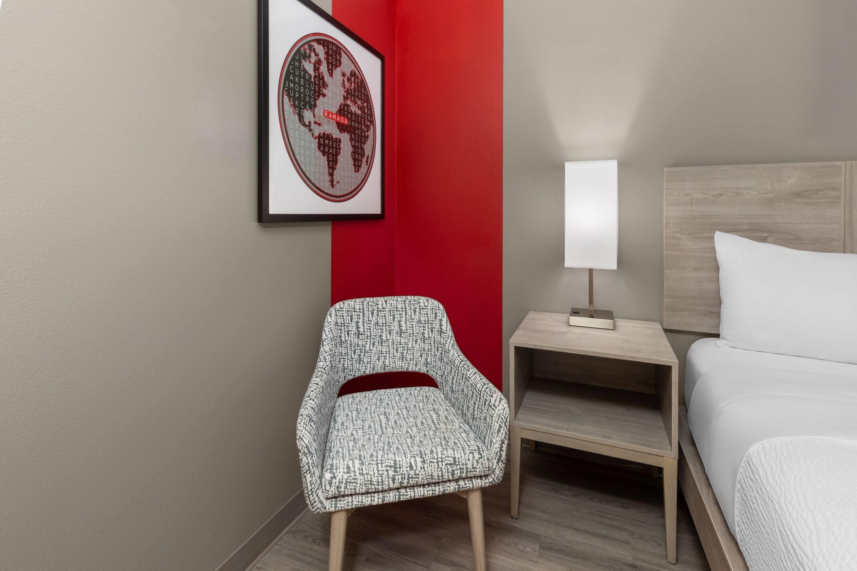 Una habitación de hotel con una cama, una silla, una mesita de noche, una lámpara y un mapa mundial enmarcado en la pared.