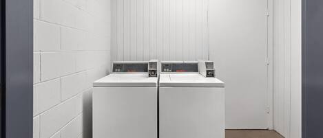 A laundry room with two white front-loading washers and dryers, white walls, and a wooden door.