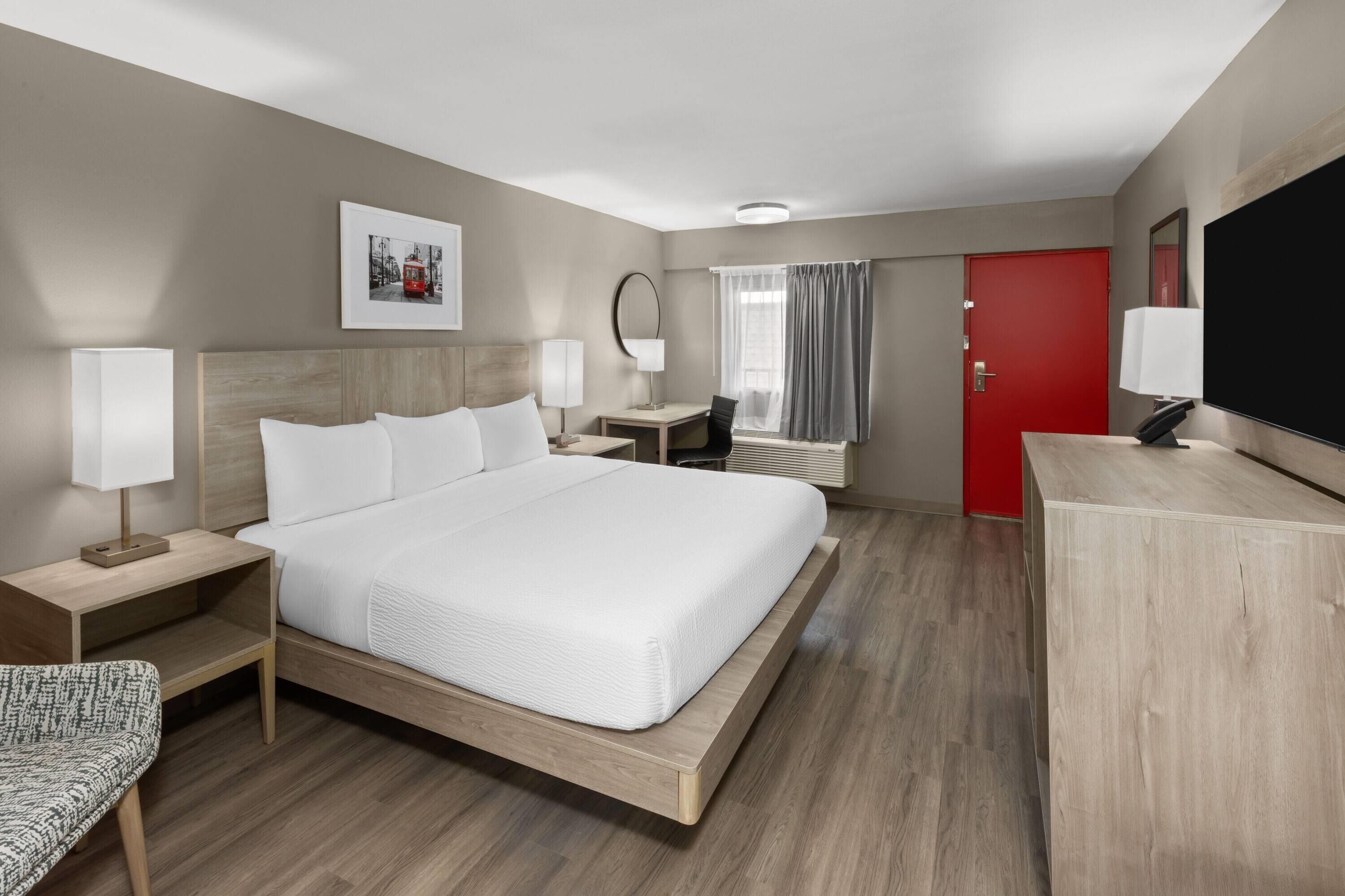 Une chambre d’hôtel moderne avec un grand lit, des tables de chevet avec des lampes, un bureau, une chaise, une télévision et une porte rouge.