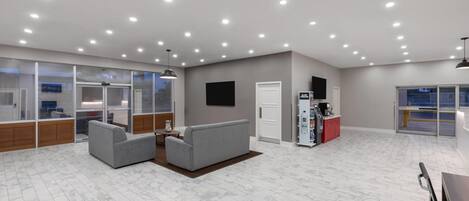 A spacious room with a grey sofa, a coffee machine, and a glass partition wall.