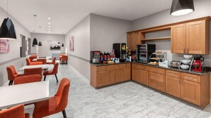 A modern kitchen with wooden cabinets, a coffee station, and orange chairs.
