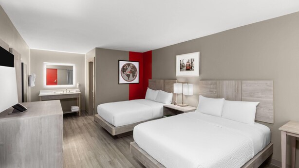 A hotel room with two beds, a desk, a mirror, and a red accent wall.
