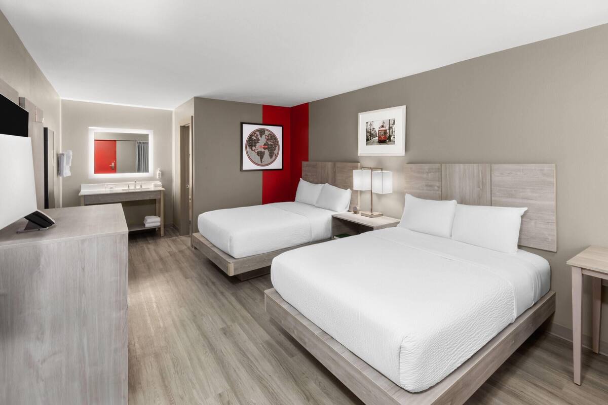 A hotel room with two beds, a desk, a mirror, and a red accent wall.