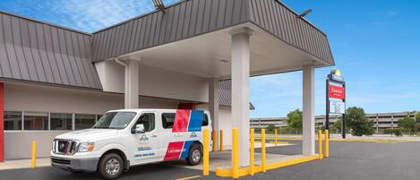 A gas station with a white van parked under a canopy, a Shell sign, and a building in the background.
