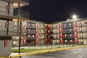 A multi-story hotel with balconies, a parking area, and a well-lit facade. - Ramada By Wyndham Kenner/New Orleans Airport South (Kenner)