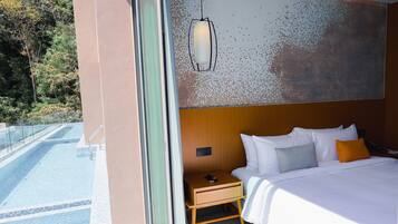 A hotel room with a bed, bedside table, and a view of a pool.