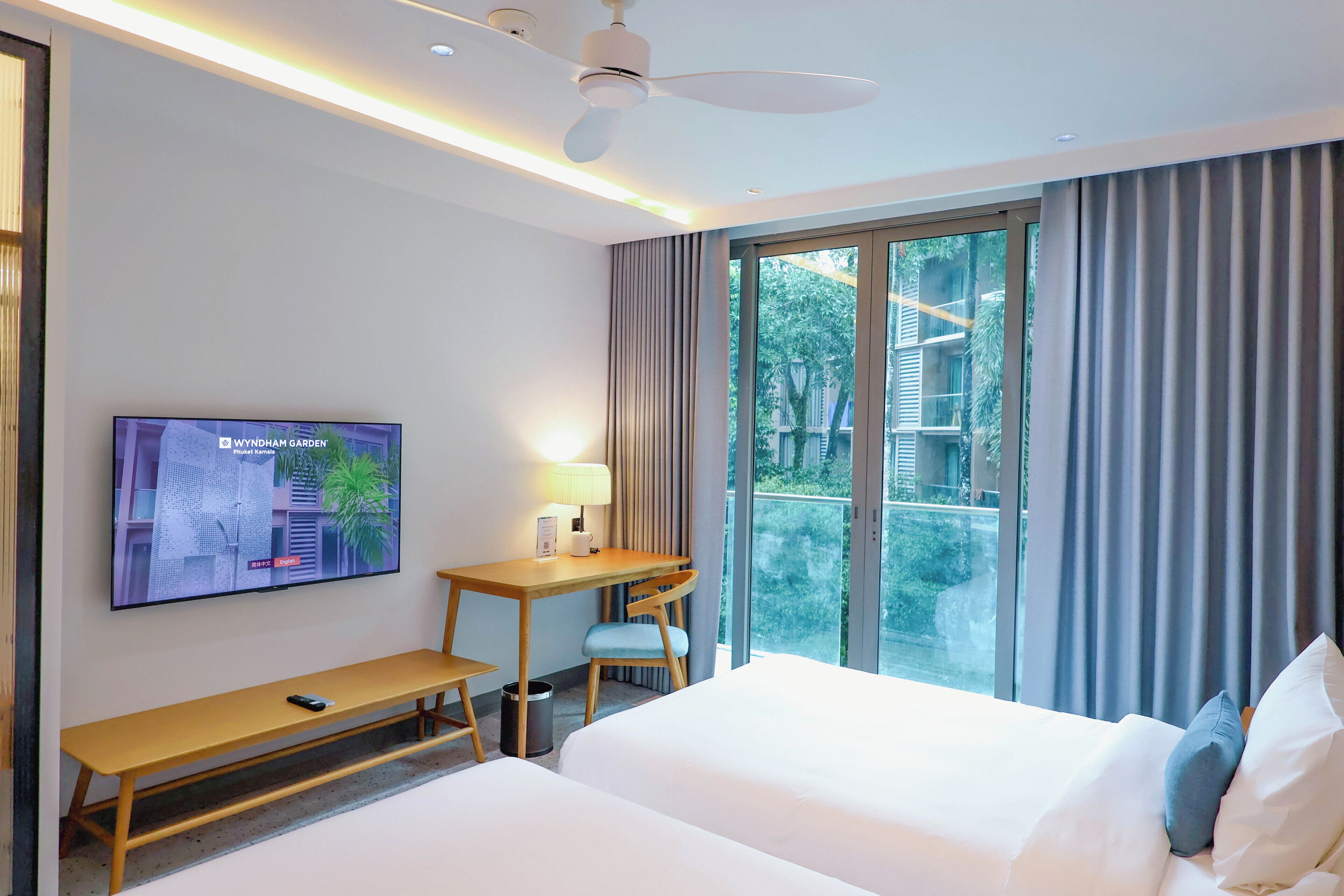 A hotel room with a bed, a desk, a chair, a TV, and a window with curtains.