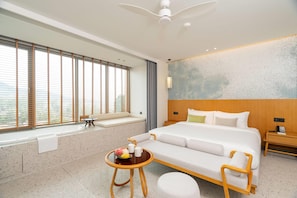 A modern hotel room with a large bed, a small table with fruit and a coffee cup, a window with blinds, and a ceiling fan. - Wyndham Garden Phuket Kamala (Kamala)
