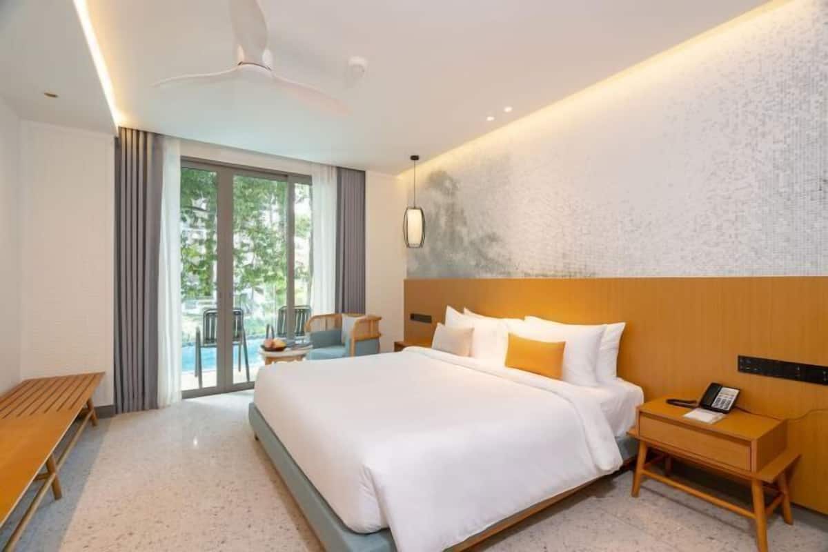 Une chambre d’hôtel avec un grand lit, une table de chevet avec un téléphone, un ventilateur de plafond et une vue sur l’extérieur grâce à une porte coulissante.