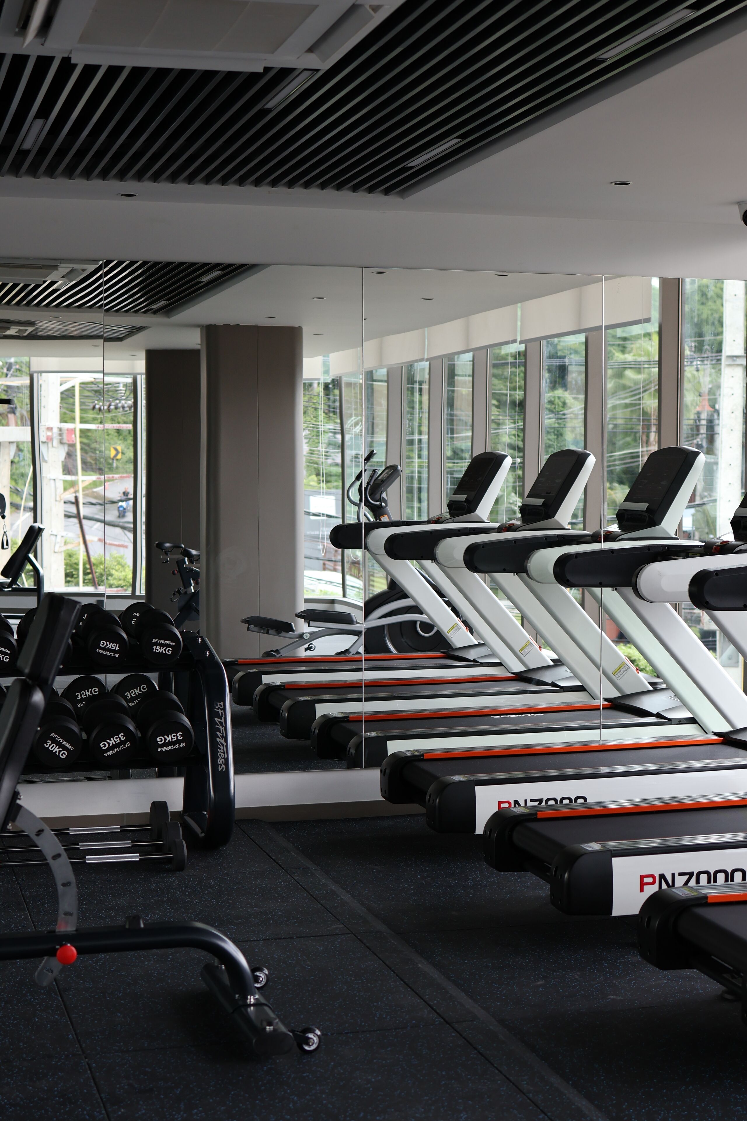 A gym with treadmills, dumbbells, and a mirror reflecting the interior.