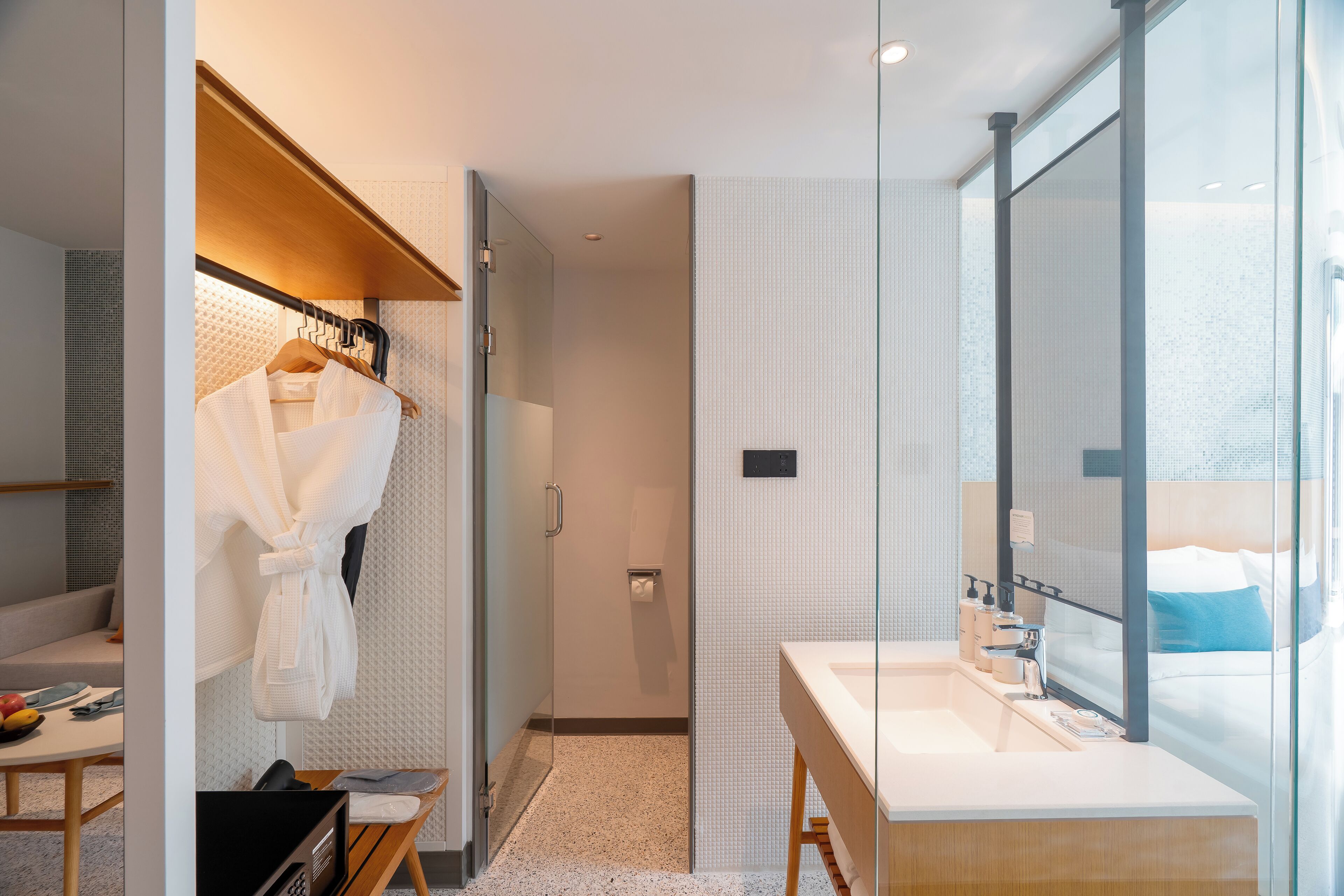 A modern bathroom with a glass shower enclosure, a white sink with a mirror, and a robe hanging on a rack.