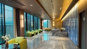 Een moderne hotellobby met een lange receptiebalie, een zithoek in groentinten en grote ramen met uitzicht.