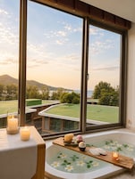 Un área de spa con bañera, velas y vistas a un campo de golf a través de amplios ventanales.