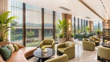 A spacious lounge area with seating, a coffee table, and large windows offering a view of greenery and mountains.