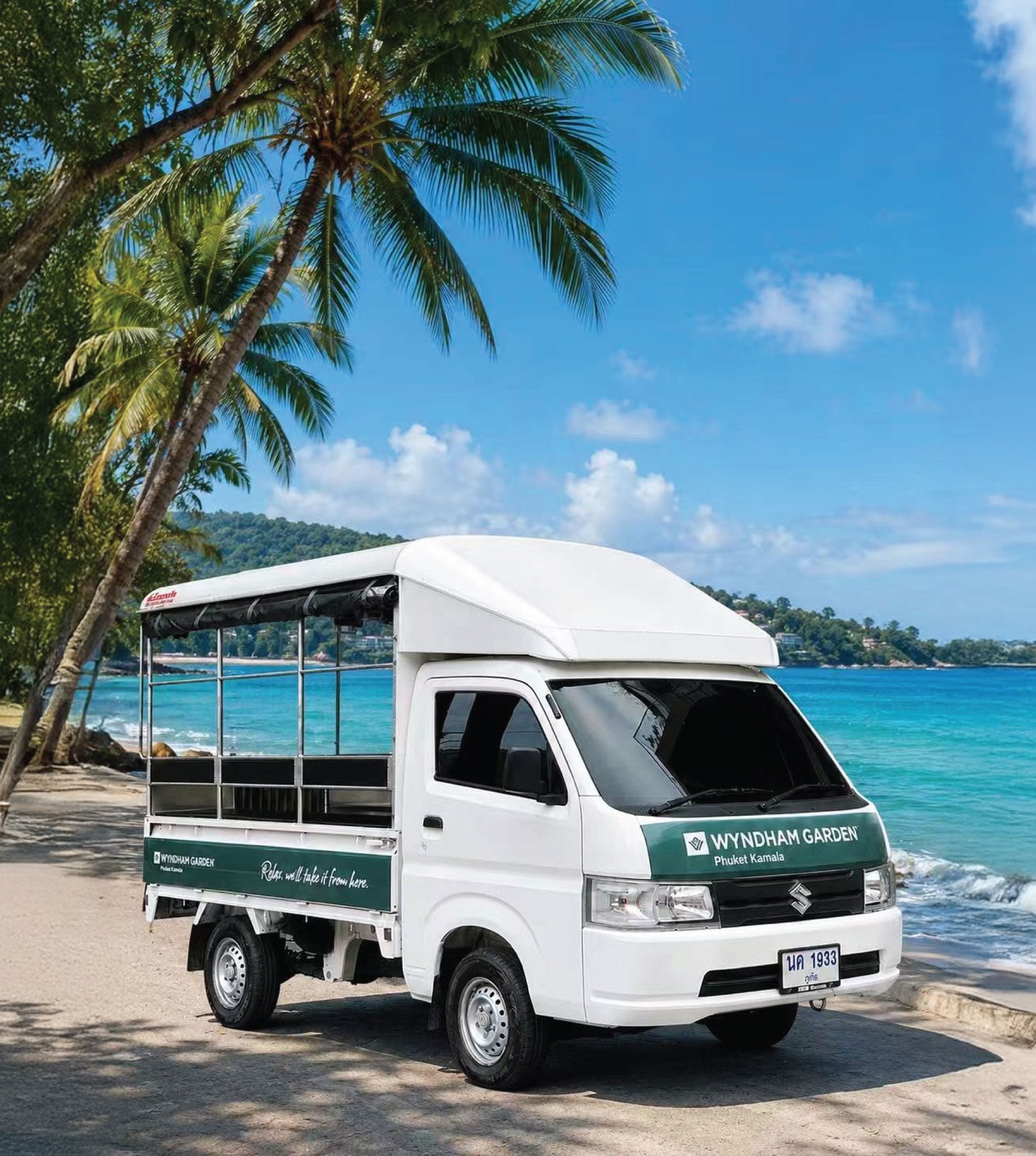 Ein weißer Van steht am Strand vor tropischer Landschaft.