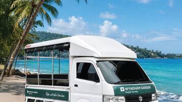 Ein weißer Van steht am Strand vor tropischer Landschaft.