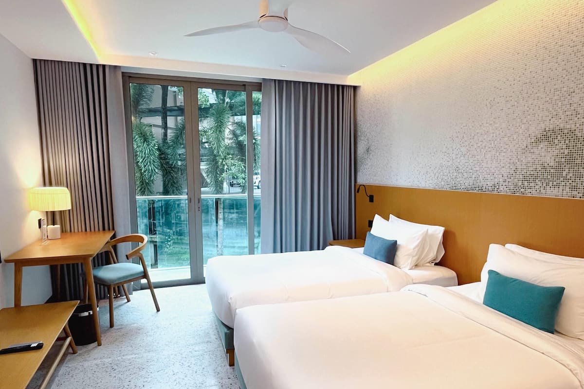 Une chambre d’hôtel avec deux lits, un bureau, une chaise et un balcon donnant sur des palmiers.